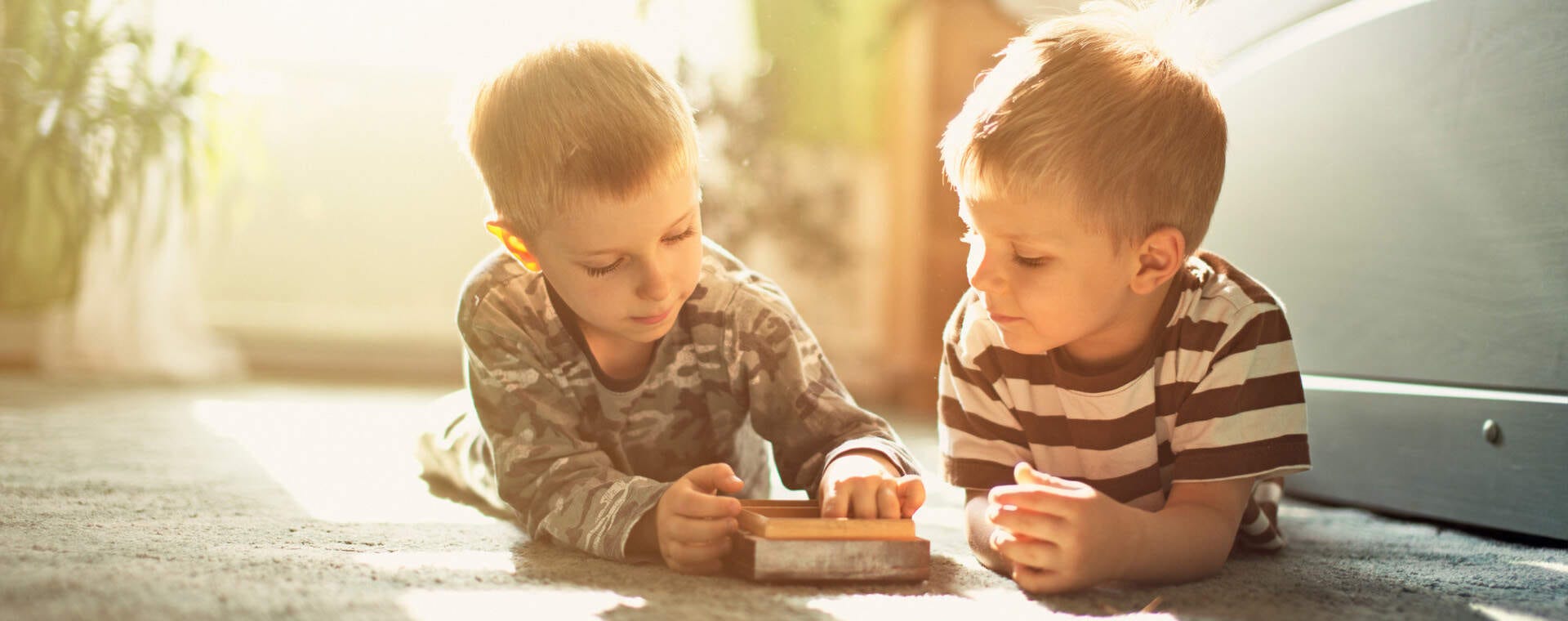 Zwei Kinder liegen auf dem Fußboden und spielen gemeinsam ein Spiel.