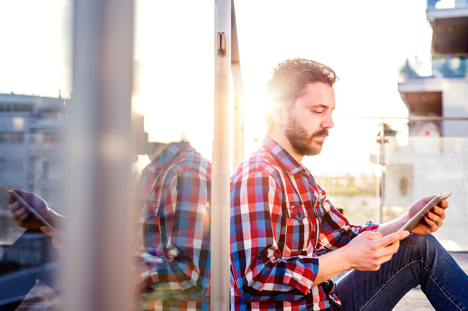 Mann sitzt an einer Fensterscheibe und schaut in sein Smartphone