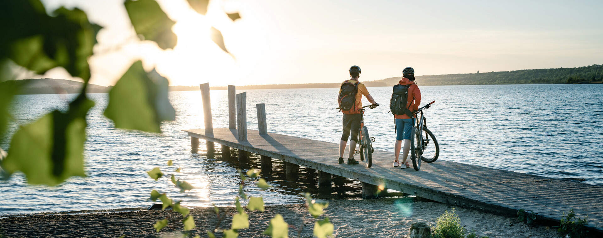 Foto - Zwei Radfahrer genießen den Sonnenuntergang auf einem Steg am See. Entspannte Abendstimmung.
